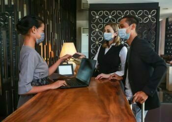 Couple and receptionist at counter in hotel wearing medical masks as precaution against virus. Couple on a business trip doing check-in at the hotel