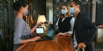Couple and receptionist at counter in hotel wearing medical masks as precaution against virus. Couple on a business trip doing check-in at the hotel